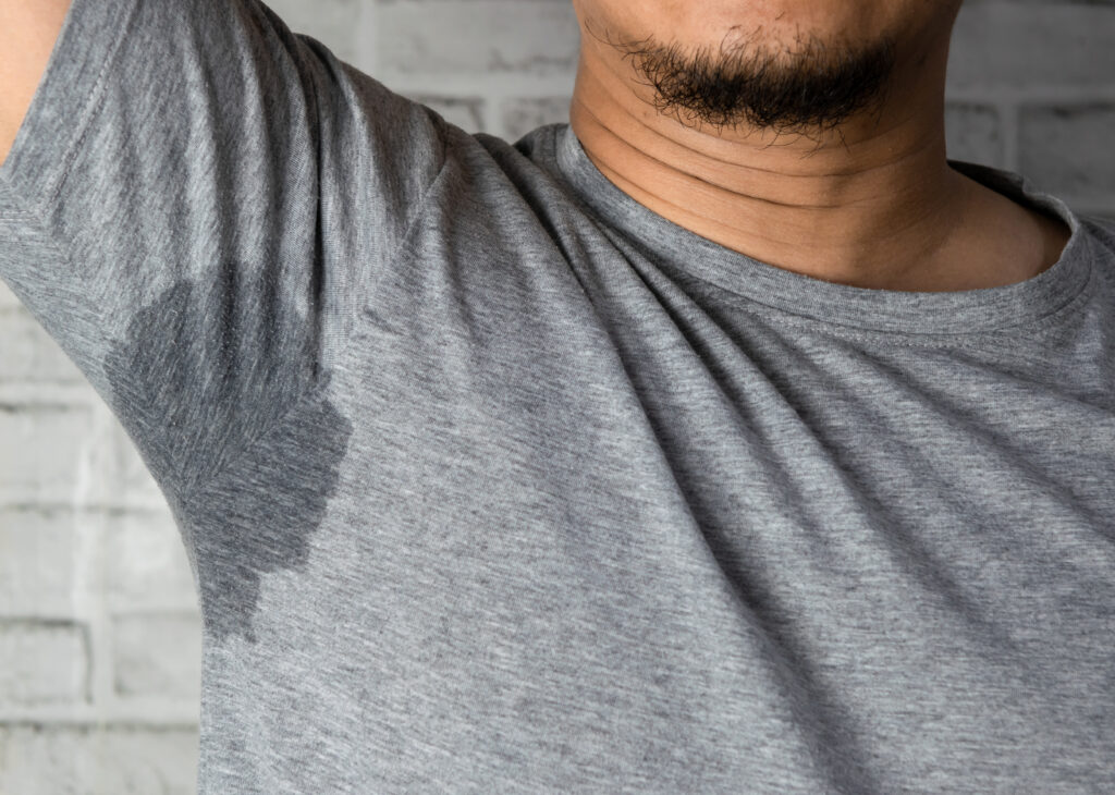 sweaty man with stain wet armpit on t shirt against gray